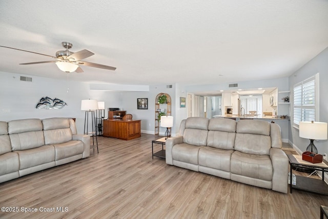 living area with light wood finished floors, visible vents, baseboards, a ceiling fan, and a textured ceiling