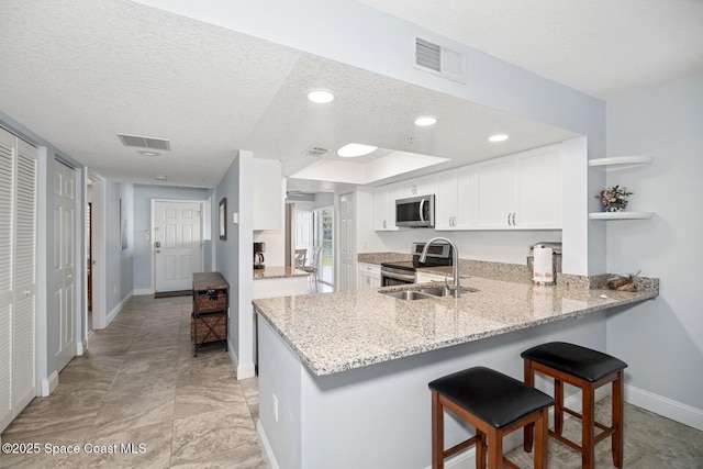 kitchen with a textured ceiling, a peninsula, appliances with stainless steel finishes, and visible vents