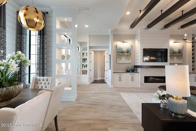 living room featuring wooden walls, beamed ceiling, ornamental molding, a high end fireplace, and light wood-type flooring