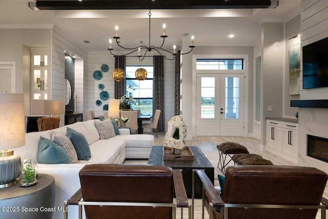 living room featuring a notable chandelier, crown molding, a high end fireplace, and french doors