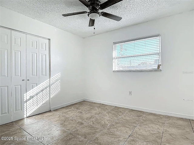 unfurnished bedroom featuring ceiling fan, light tile patterned floors, a textured ceiling, and a closet