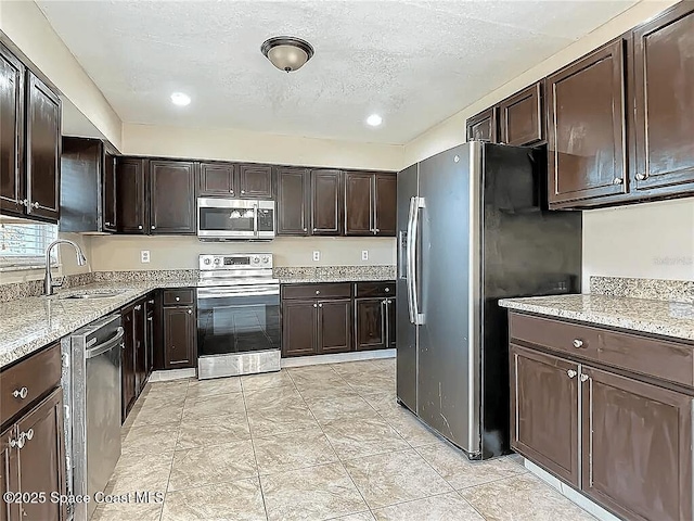 kitchen with stainless steel appliances, dark brown cabinets, sink, and light stone counters