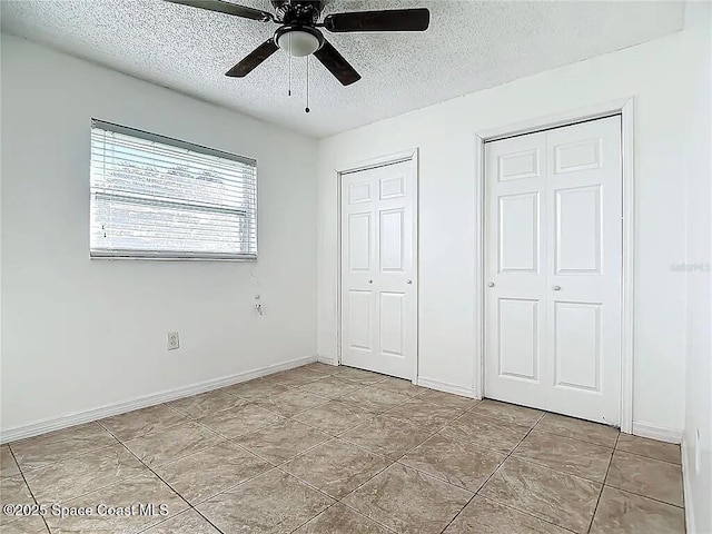 unfurnished bedroom featuring ceiling fan, a textured ceiling, and two closets