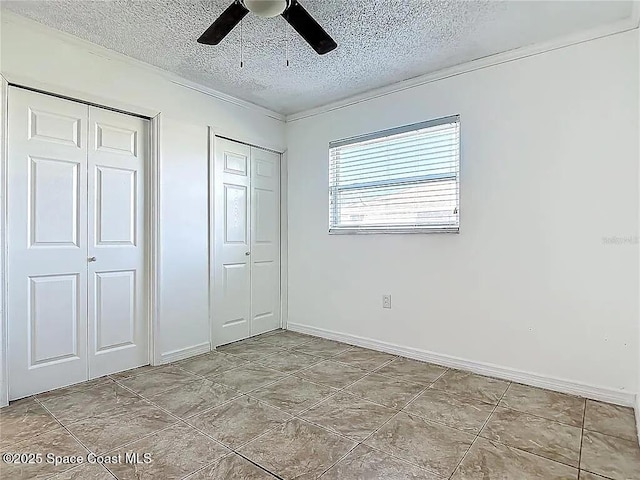 unfurnished bedroom featuring ceiling fan, a textured ceiling, and two closets