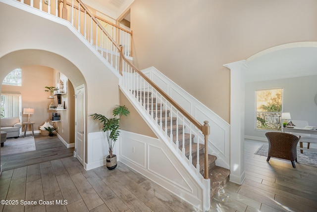 staircase featuring arched walkways, a decorative wall, a high ceiling, and wood finished floors