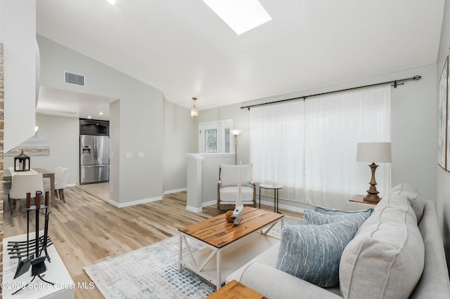 living room featuring lofted ceiling with skylight and light hardwood / wood-style flooring