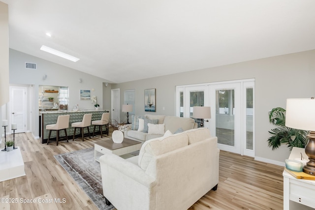 living room featuring a healthy amount of sunlight, light hardwood / wood-style flooring, french doors, and vaulted ceiling with skylight