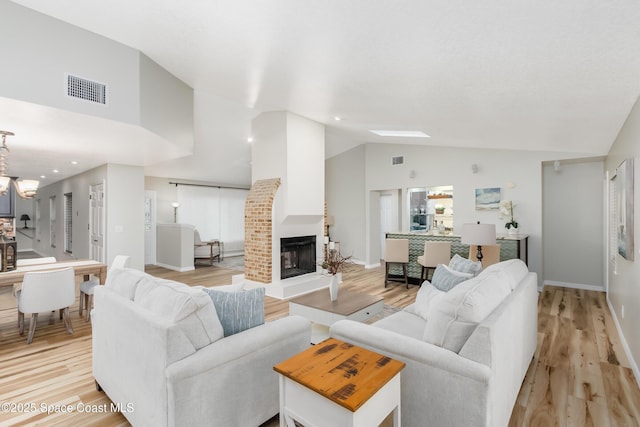 living room featuring lofted ceiling, a brick fireplace, a chandelier, and light wood-type flooring