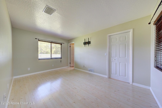 empty room featuring a textured ceiling and light hardwood / wood-style flooring