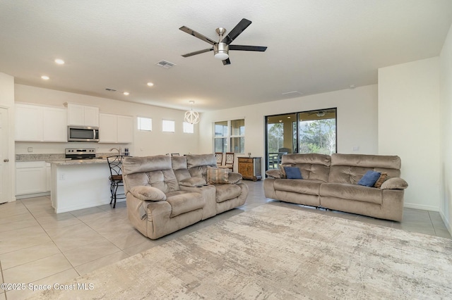 tiled living room with ceiling fan with notable chandelier