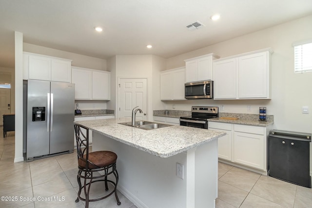 kitchen with sink, appliances with stainless steel finishes, an island with sink, light stone countertops, and white cabinets