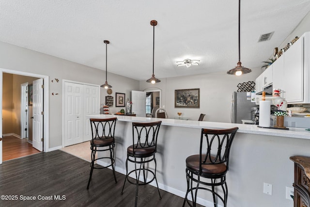 kitchen with dark wood-type flooring, a breakfast bar area, white cabinetry, decorative light fixtures, and kitchen peninsula