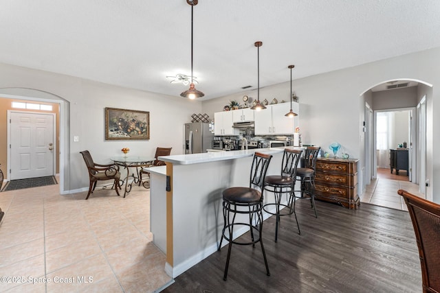 kitchen featuring pendant lighting, a kitchen breakfast bar, white cabinets, stainless steel fridge with ice dispenser, and kitchen peninsula