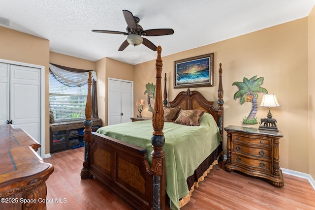 bedroom featuring hardwood / wood-style flooring, ceiling fan, multiple closets, and a textured ceiling