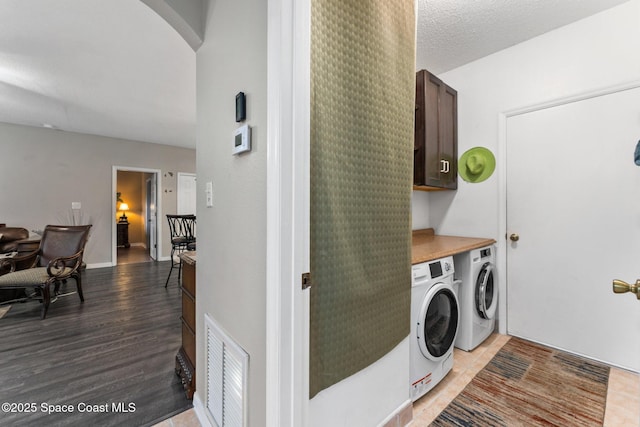 laundry area featuring cabinets, washing machine and dryer, a textured ceiling, and light hardwood / wood-style floors