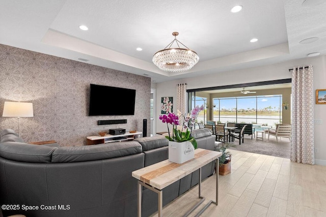 living room with an inviting chandelier, a tray ceiling, and light hardwood / wood-style floors