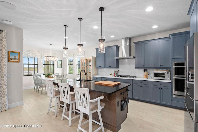 kitchen with pendant lighting, a breakfast bar area, backsplash, an island with sink, and wall chimney exhaust hood