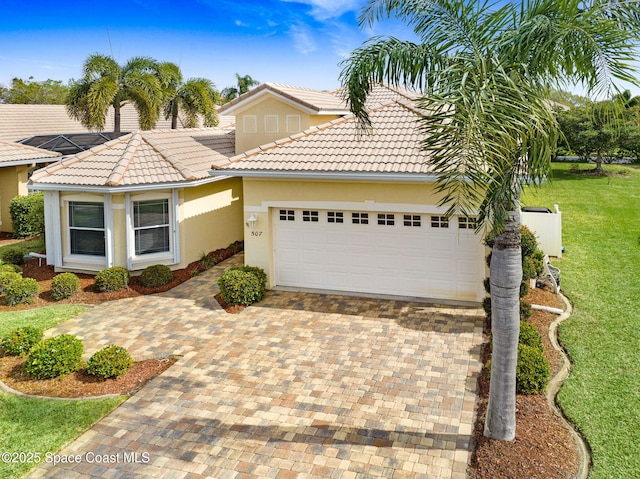 mediterranean / spanish-style house featuring decorative driveway, a tile roof, stucco siding, an attached garage, and a front lawn