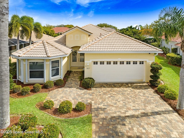 mediterranean / spanish house with a tiled roof, an attached garage, decorative driveway, a front yard, and stucco siding