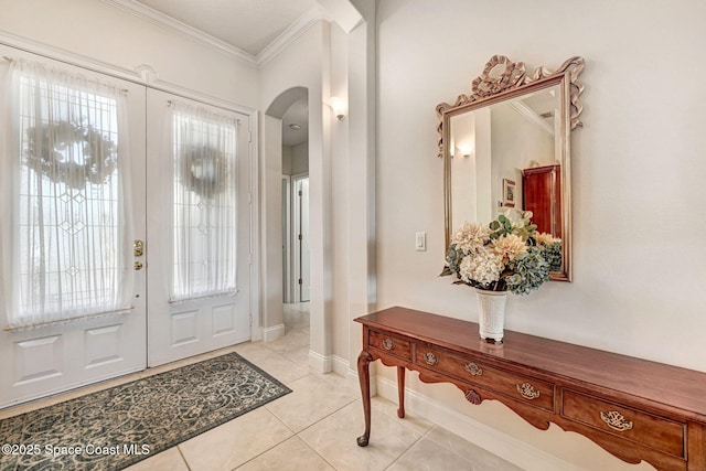 foyer with ornamental molding, arched walkways, french doors, and light tile patterned floors