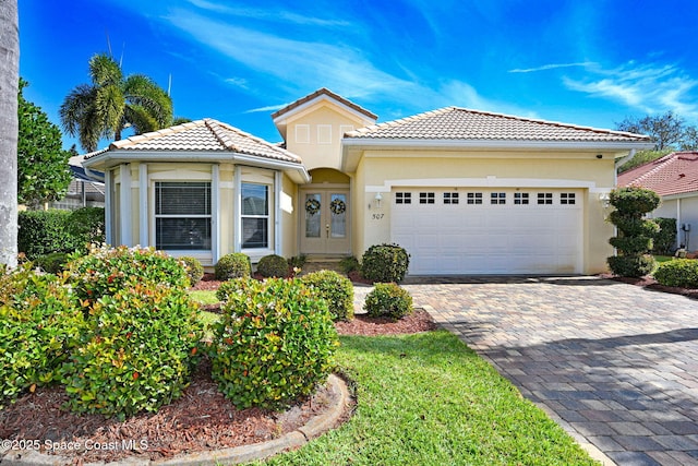 view of front of home with decorative driveway, french doors, a tile roof, stucco siding, and a garage