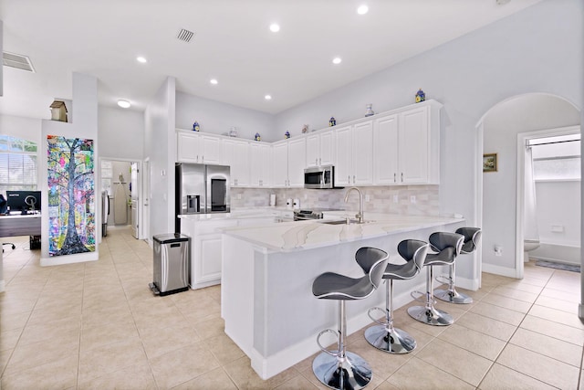 kitchen featuring stainless steel appliances, white cabinets, light stone counters, and kitchen peninsula