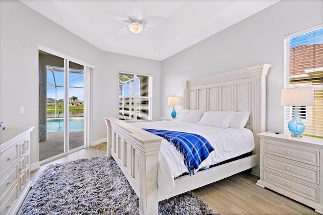 bedroom featuring a tray ceiling, access to outside, light hardwood / wood-style floors, and ceiling fan