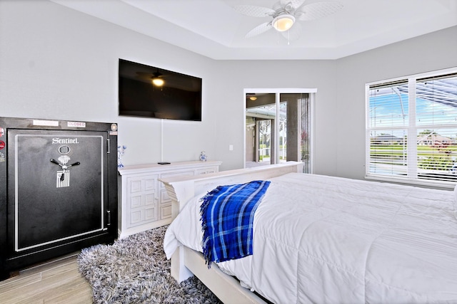 bedroom featuring multiple windows, light hardwood / wood-style flooring, a raised ceiling, and ceiling fan