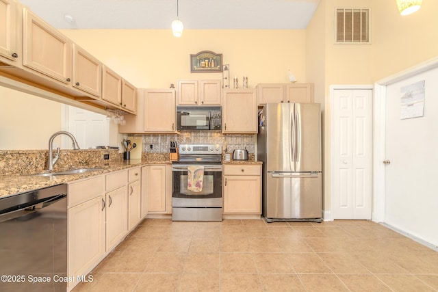 kitchen with a towering ceiling, decorative light fixtures, black appliances, light stone countertops, and decorative backsplash