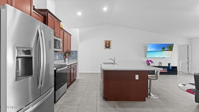 kitchen featuring sink, a breakfast bar, stainless steel appliances, an island with sink, and vaulted ceiling