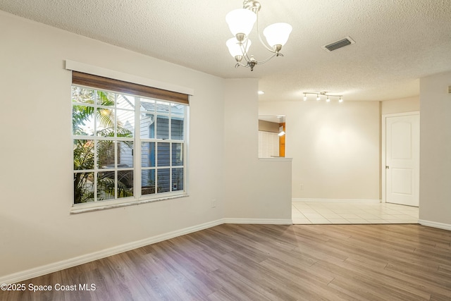 spare room with a chandelier, light hardwood / wood-style floors, and a textured ceiling