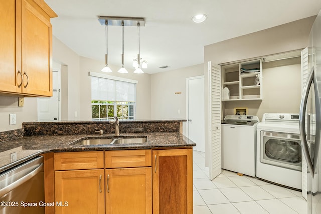 kitchen with pendant lighting, sink, dark stone counters, stainless steel appliances, and washing machine and dryer