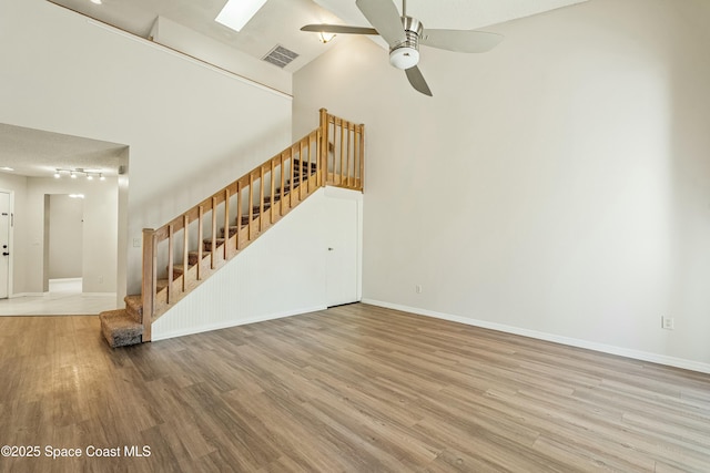 unfurnished living room with ceiling fan, track lighting, hardwood / wood-style floors, and a high ceiling