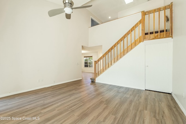 unfurnished living room with hardwood / wood-style flooring, ceiling fan, and a towering ceiling