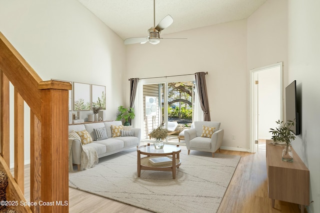 living room with ceiling fan, high vaulted ceiling, a textured ceiling, and light wood-type flooring