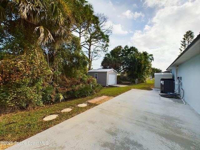 view of yard with a detached garage, central air condition unit, concrete driveway, a patio area, and an outdoor structure