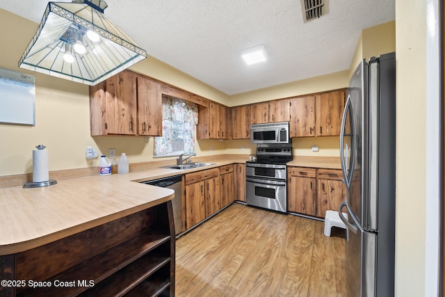 kitchen with appliances with stainless steel finishes, sink, a textured ceiling, and light hardwood / wood-style flooring