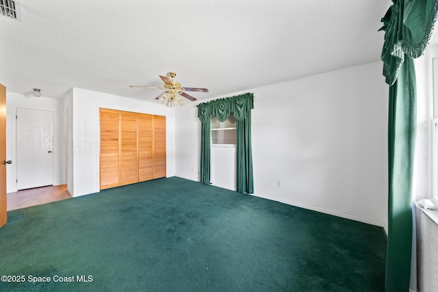 unfurnished bedroom with ceiling fan, a closet, a textured ceiling, and dark colored carpet