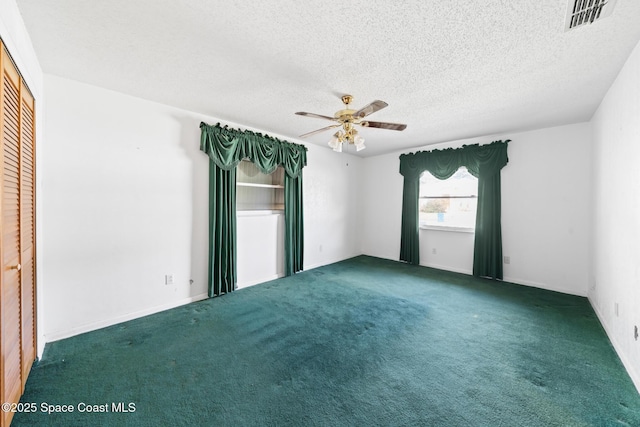 spare room featuring ceiling fan, dark carpet, and a textured ceiling