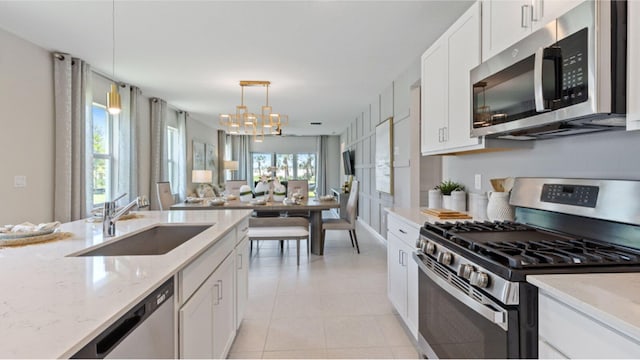 kitchen featuring stainless steel appliances, hanging light fixtures, white cabinetry, a sink, and light stone countertops