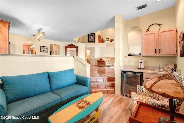 living room with lofted ceiling, sink, beverage cooler, and light wood-type flooring