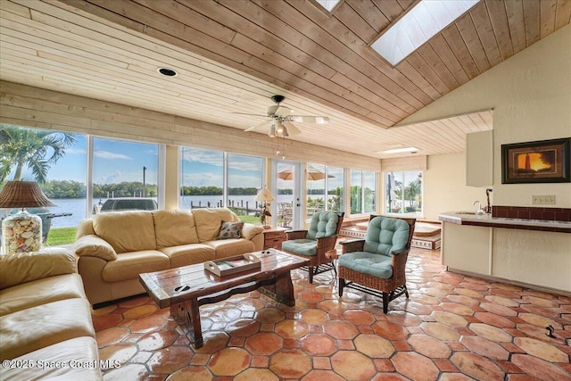 living room featuring sink, a water view, wooden ceiling, ceiling fan, and vaulted ceiling with skylight