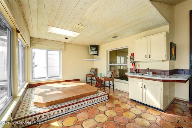 kitchen with light tile patterned floors, white cabinetry, a skylight, tile countertops, and wooden ceiling