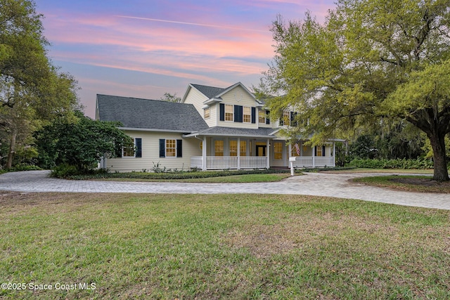 view of front of home with covered porch, driveway, a shingled roof, and a lawn