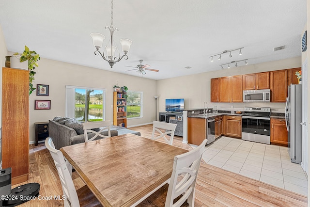 dining space featuring sink, ceiling fan with notable chandelier, and light wood-type flooring