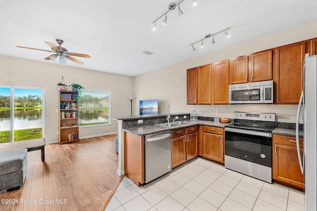 kitchen featuring sink, appliances with stainless steel finishes, a water view, a healthy amount of sunlight, and kitchen peninsula