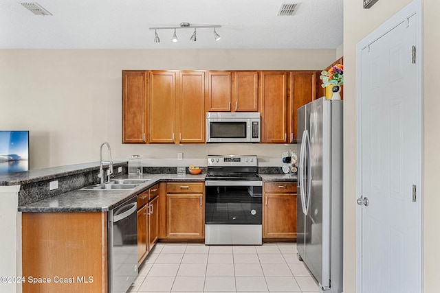 kitchen with sink, light tile patterned floors, appliances with stainless steel finishes, a textured ceiling, and kitchen peninsula