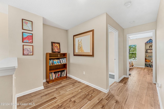 hall with a textured ceiling and light wood-type flooring