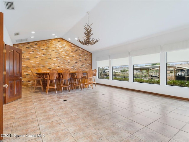 interior space featuring lofted ceiling, bar area, light tile patterned floors, a notable chandelier, and brick wall