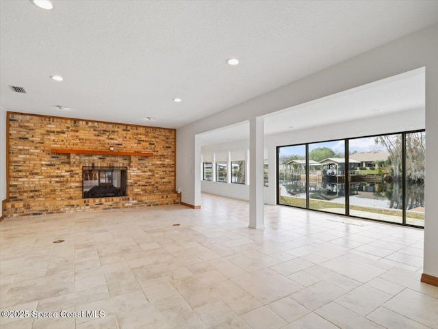 unfurnished living room featuring brick wall, a water view, a textured ceiling, and a brick fireplace